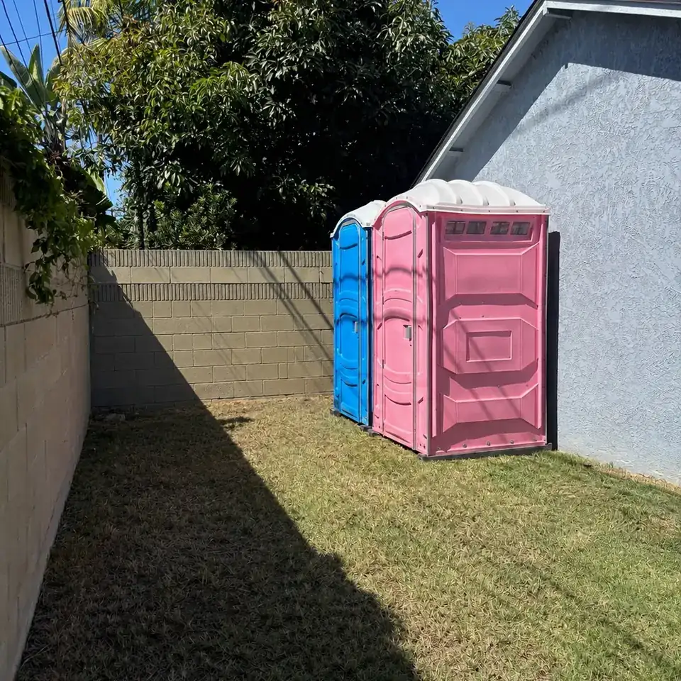 Two porta potties in a fenced backyard