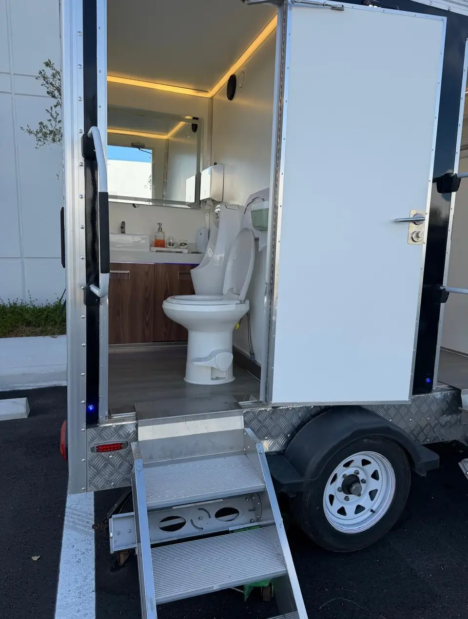 Restroom trailer door open with metal steps and a lit interior