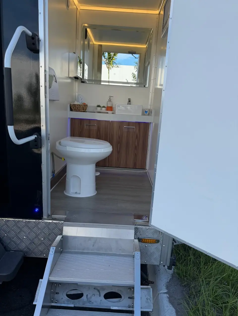 Restroom trailer door open showing a flushing toilet and vanity inside