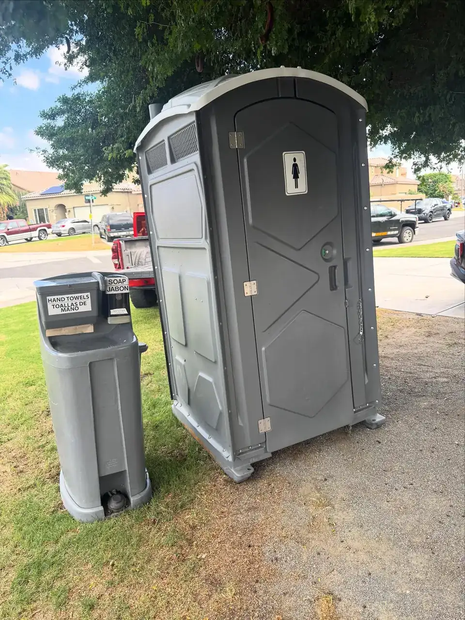 Gray porta potty with a hand-wash station on a lawn, the kind of unit delivered in Wagoner
