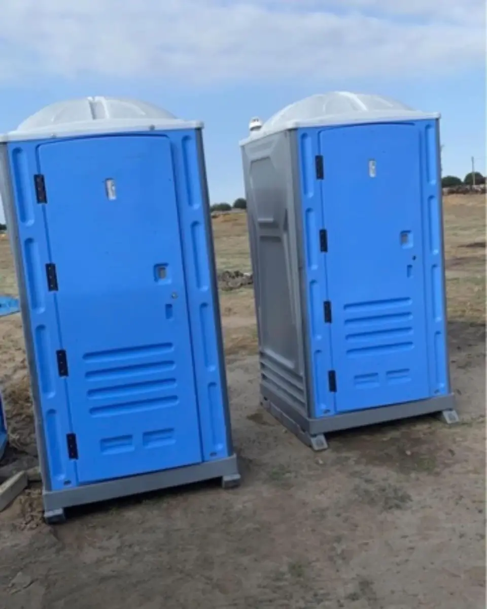 Two blue standard porta potties on open ground