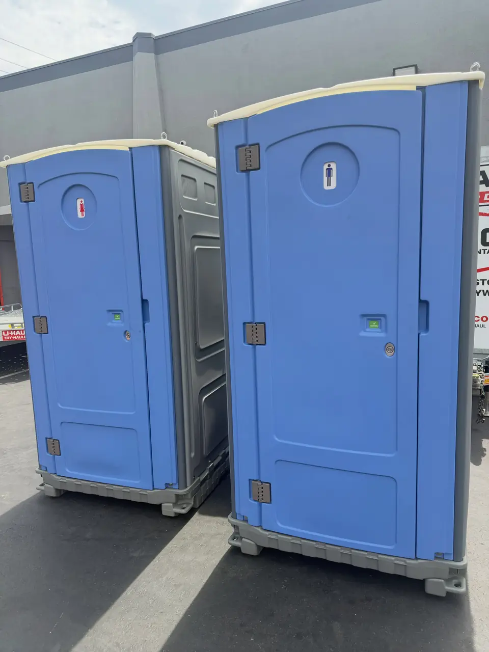 Two blue porta potties on a gravel lot